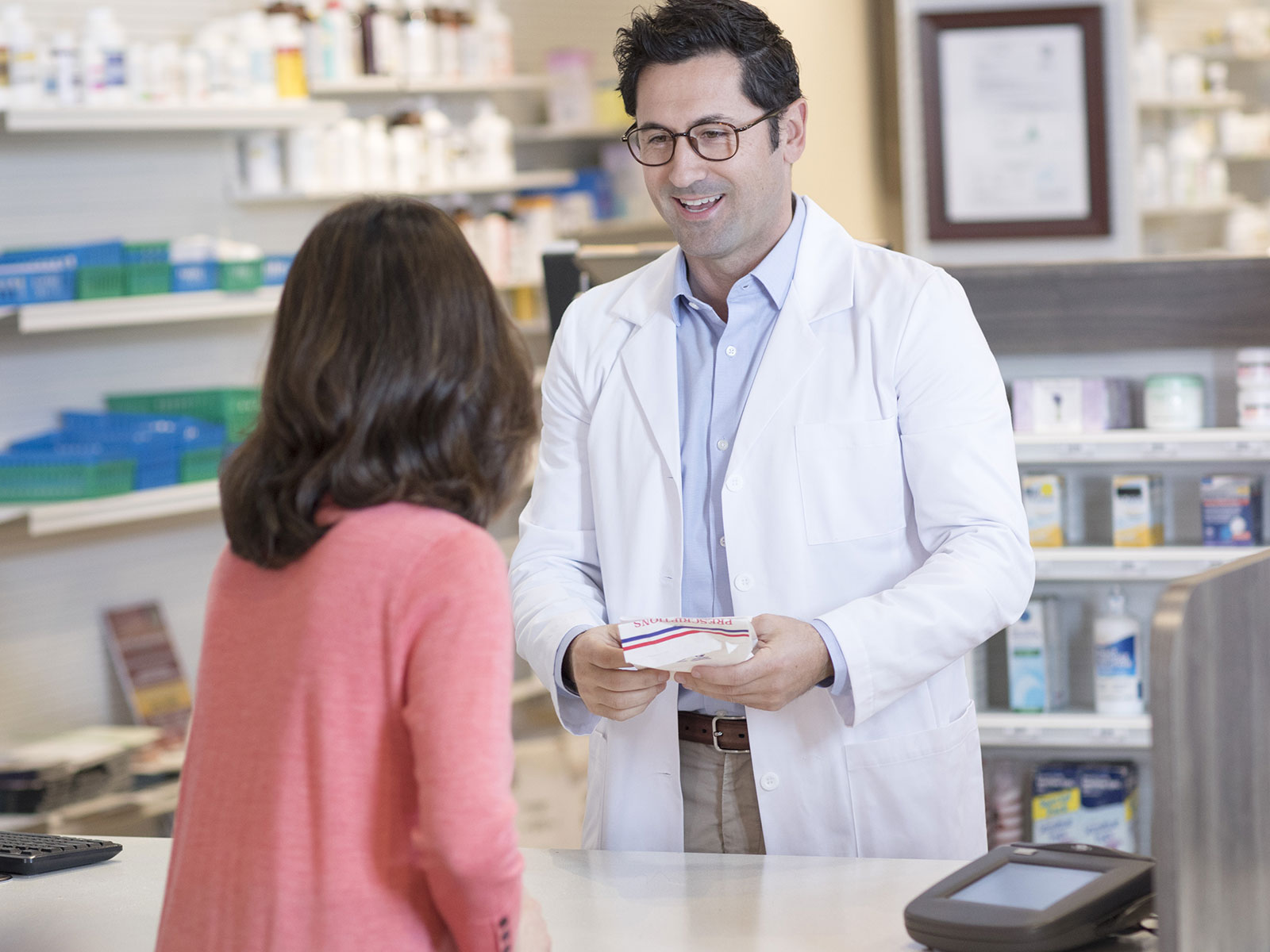 Male pharmacist helps female customer at counter.